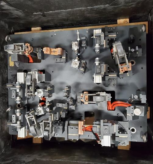 Fixture with multiple metal clamping mechanisms on a dark surface, likely for holding parts during manufacturing.