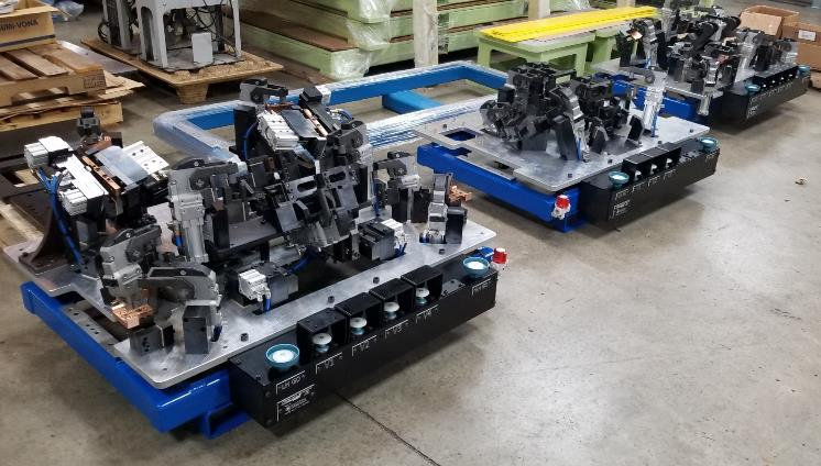 Three industrial workstations with black and silver fixtures, on blue carts in a factory setting.
