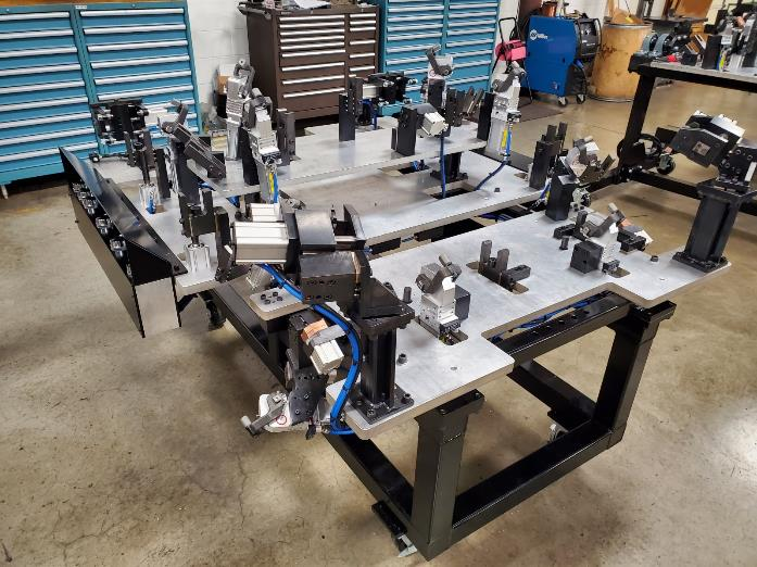 Metal fabrication jig with clamps and supports on a steel frame, in a workshop setting.