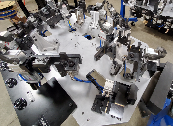 A large, complex industrial jig on a workbench; multiple black and silver clamps secure parts.
