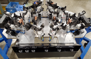 Complex industrial jig with multiple clamps and supports, mounted on a blue frame.