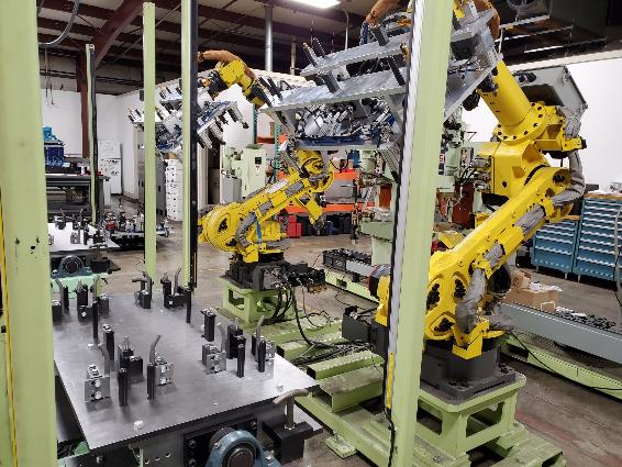 Yellow robotic arms assembling parts in an industrial setting, with a metal table and various machinery.