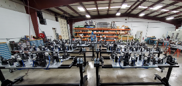 A large industrial workshop with multiple machines on tables. Shelves of materials and tools are in the background.