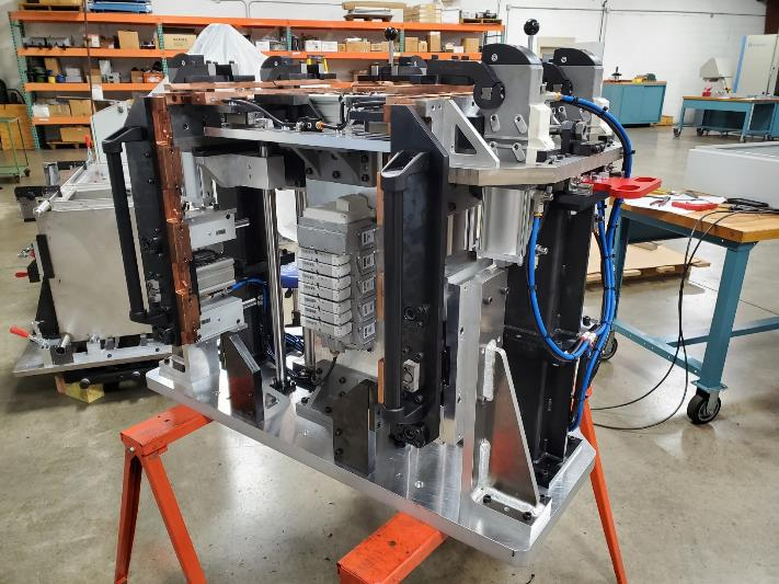 Complex industrial machine on an orange stand, in a workshop setting.