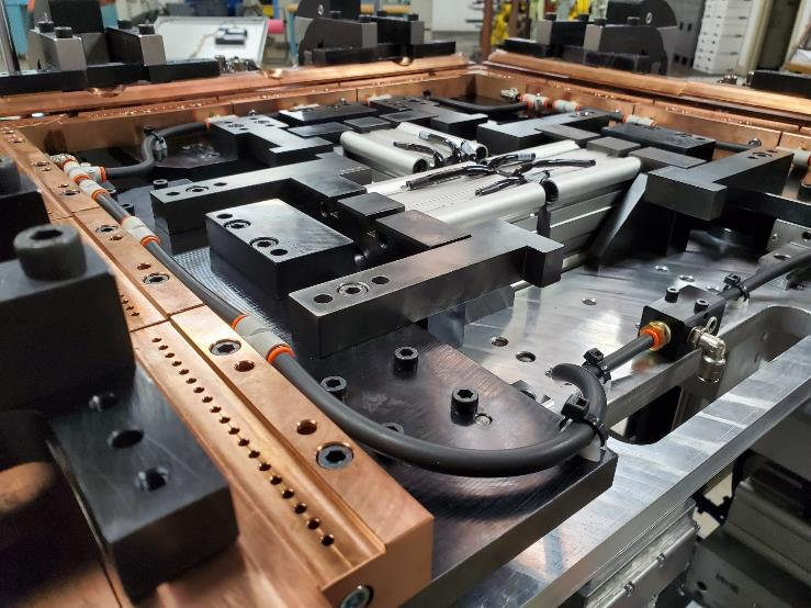 Metal industrial fixture with copper and black components, tubing, and mounting blocks.