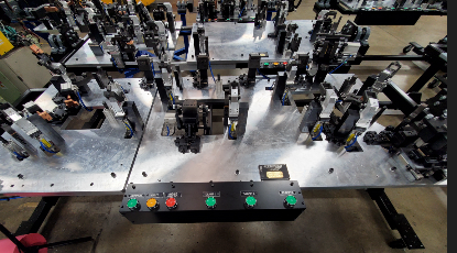 Control panel with buttons on a machine with various clamps and mounts on a metal surface.