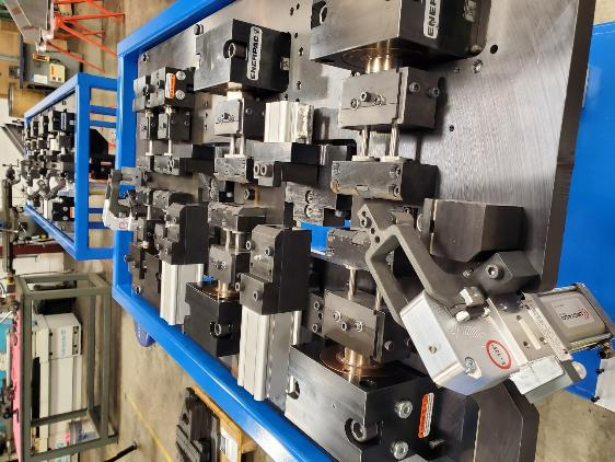 Metal fixture with numerous clamps and blocks, likely for holding parts during manufacturing, in a workshop setting.