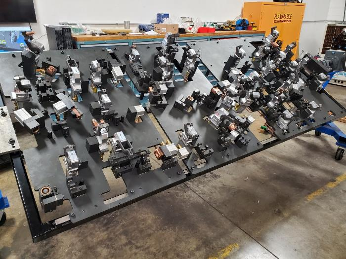 Large black industrial jig with various clamps and fixtures, likely for manufacturing, on a shop floor.