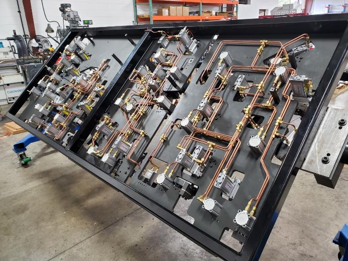 Black metal panel with complex copper tubing and machinery. Industrial setting.