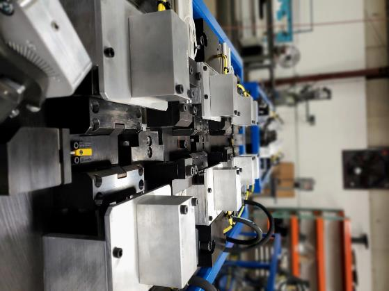 Close-up of a metal fabrication machine, featuring multiple adjustable clamps and tooling, indoors.