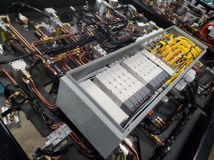 Open metal box revealing circuit boards, connected by wires and yellow cables, within a larger electronic assembly.