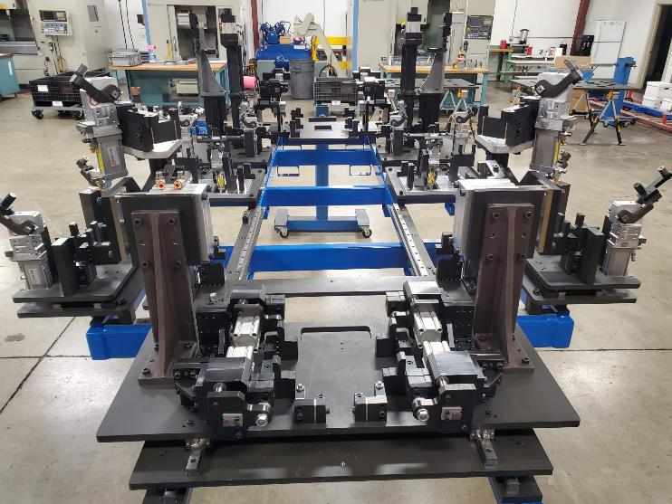 Automotive welding fixture in a factory, holding multiple components for assembly. Mostly black and blue with silver components.