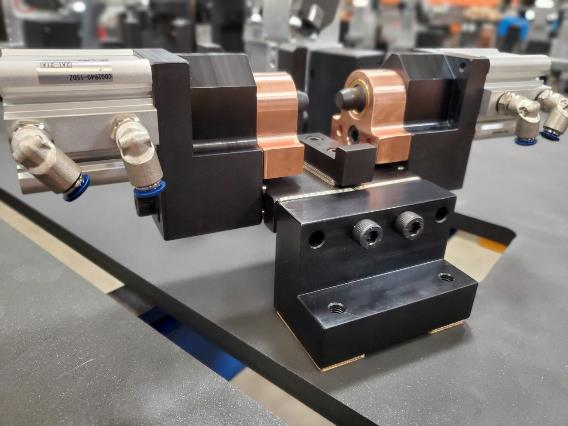 Welding fixture with copper components and pneumatic cylinders on a table.