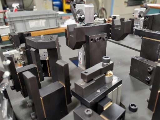 Close-up of a black metal fixture with various clamps, used in manufacturing, resting on a gray surface.