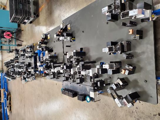 A large industrial work surface with numerous small metal and plastic components attached; a factory setting.