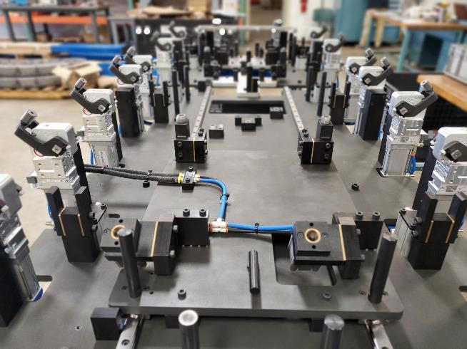 Black and grey metal industrial fixture with numerous posts, levers, and wiring in a manufacturing setting.