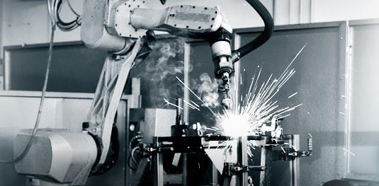 A robotic arm welding metal with sparks and smoke in a factory setting.