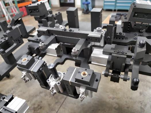 Industrial assembly fixture with black metal components, silver base, and pneumatic cylinders.