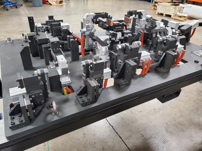 Complex black and silver industrial jig, with various clamps and fixtures, on a metal base, indoors.