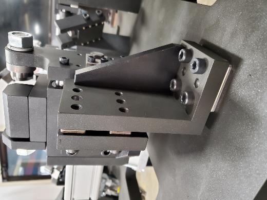Close-up of a dark metal angled bracket with drilled holes attached to a machine.
