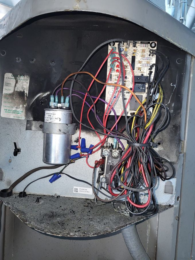 Open electrical panel with tangled red and black wires and a metal component inside a gray enclosure