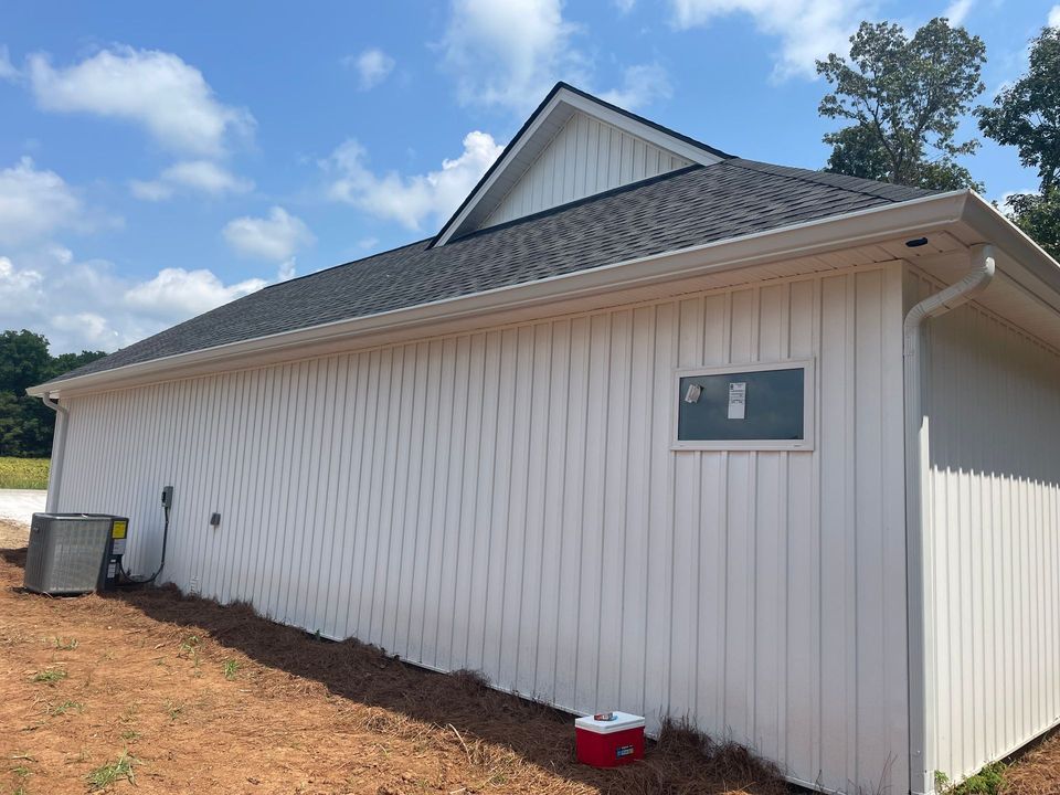 White-sided building with a dark roof and small window on a dirt lot under a blue sky