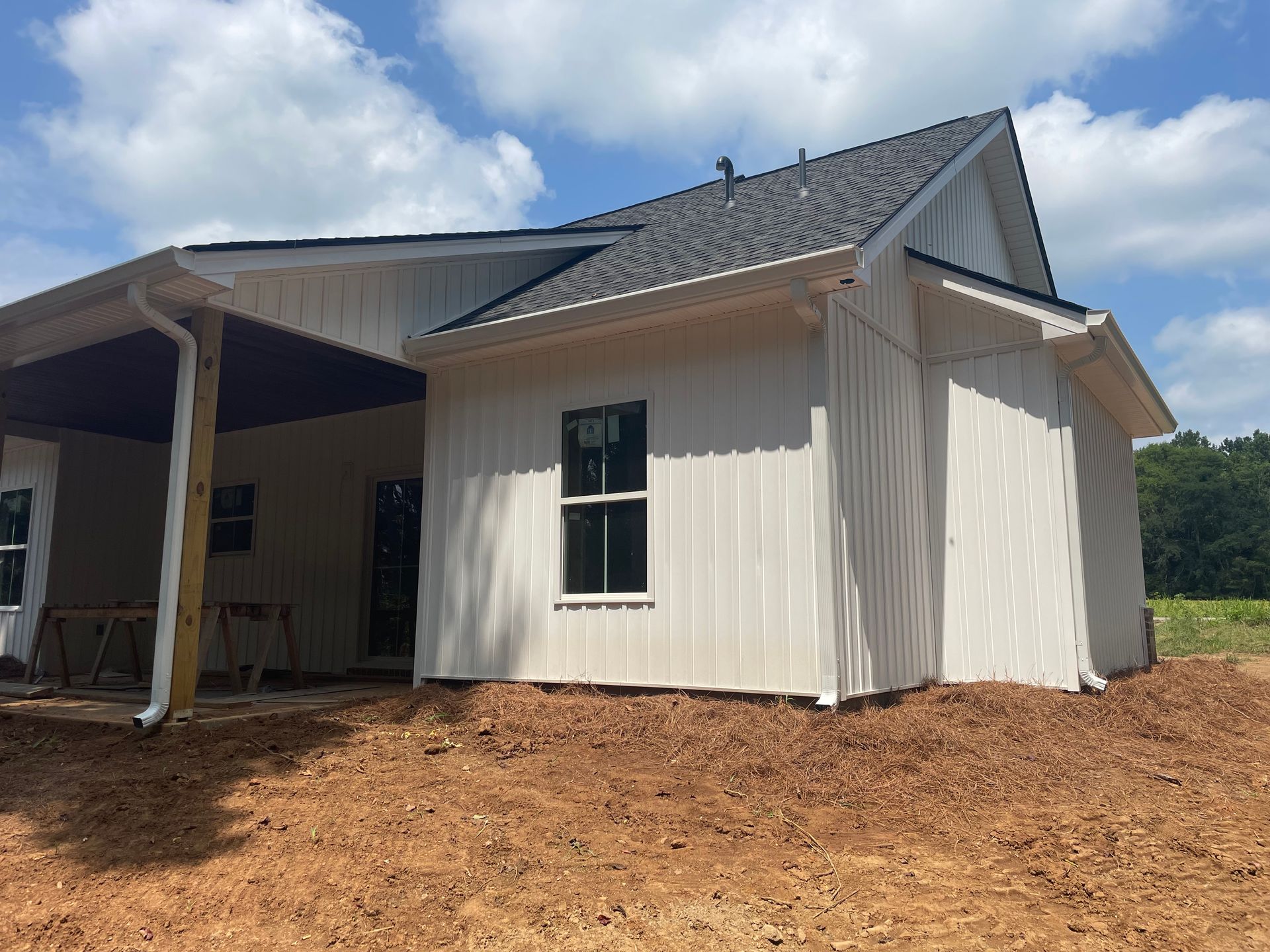 New white house exterior with gray roof and covered porch on bare dirt lot
