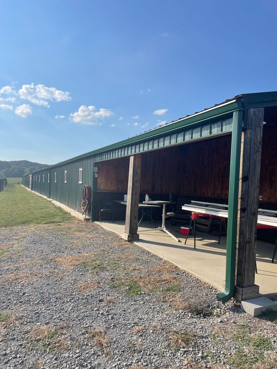 Long covered outdoor storage bay with green roof, gravel foreground, and red equipment inside under blue sky