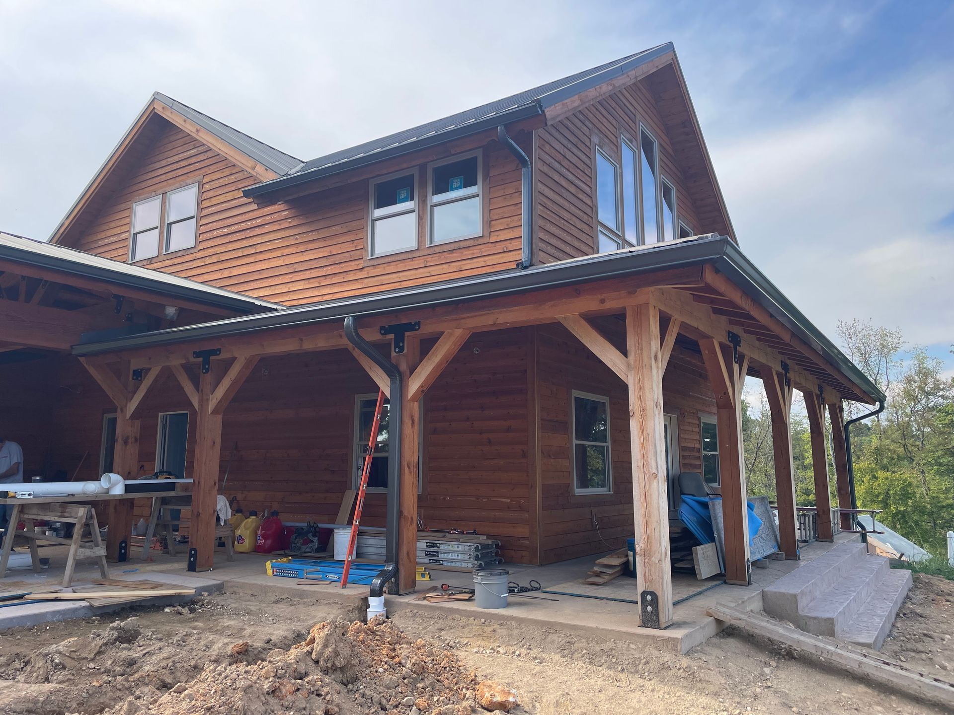 Wooden house under construction with porch posts, brick upper walls, and scattered building materials outside.