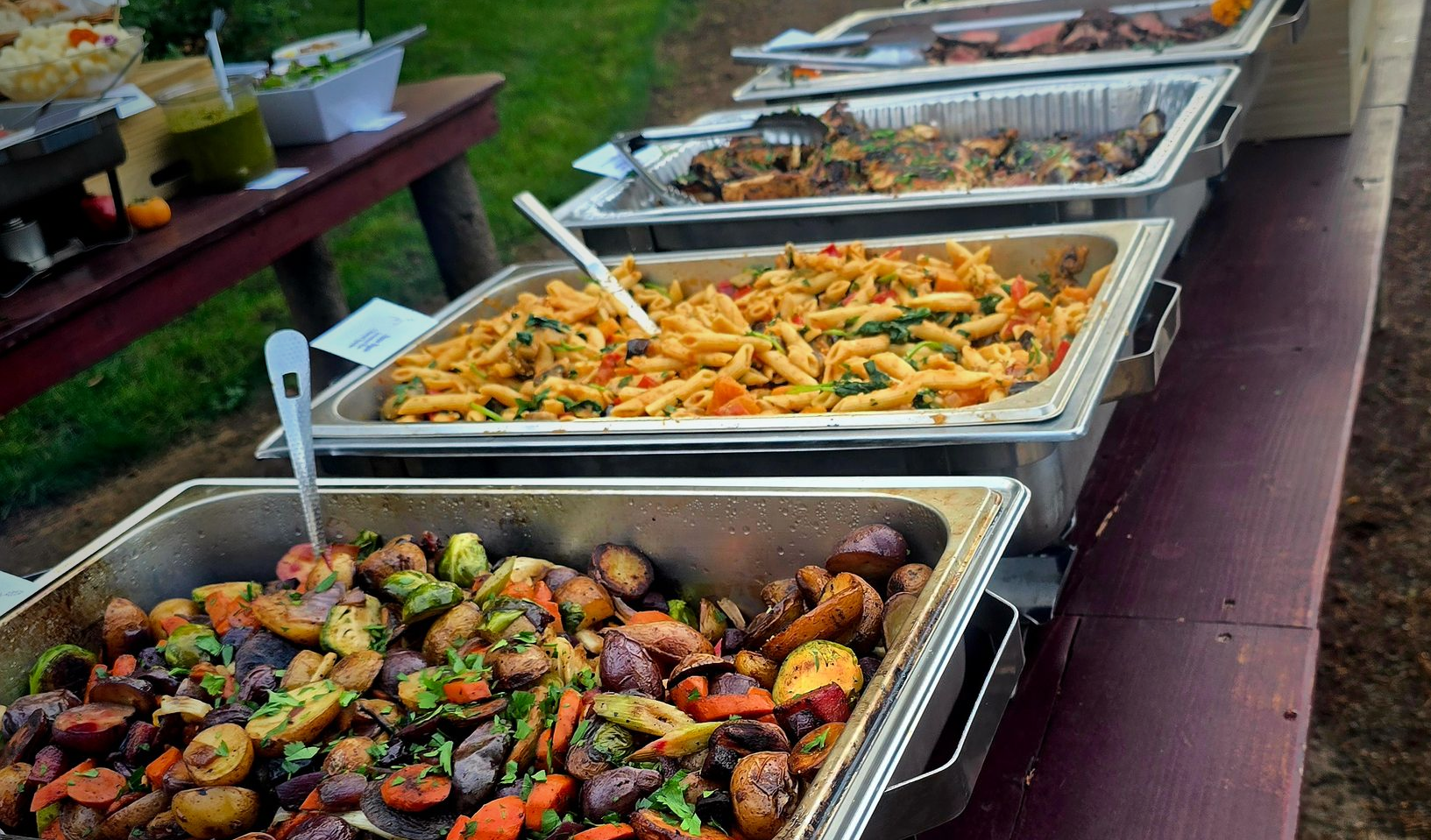 Buffet table with trays of assorted roasted vegetables and salads at an outdoor gathering