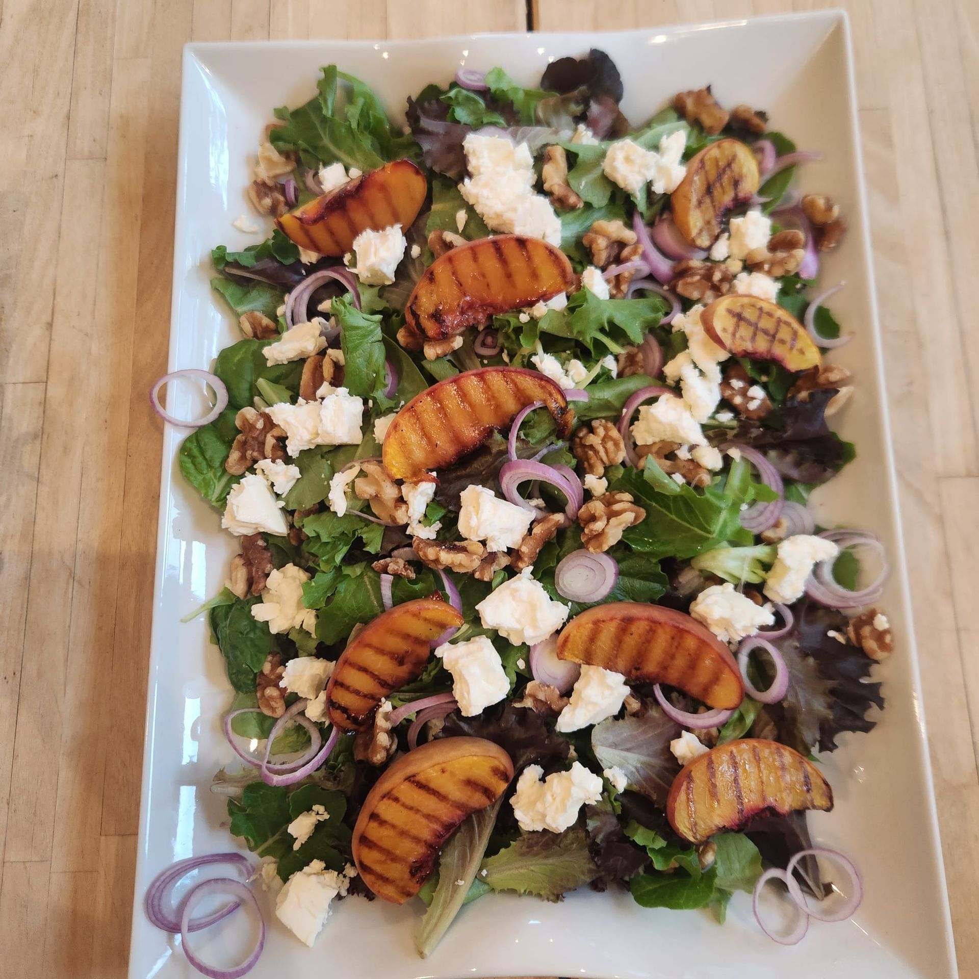 Plated salad with grilled peaches, feta, red onions, walnuts, and mixed greens