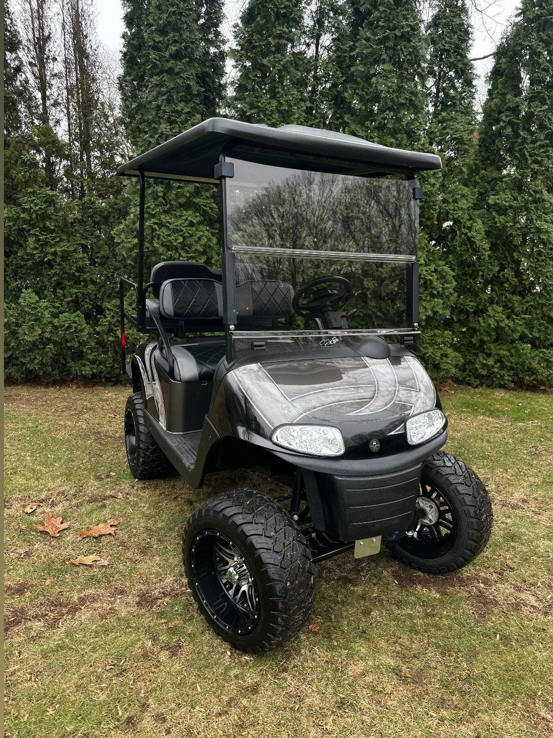A golf cart is parked in the grass in front of trees.