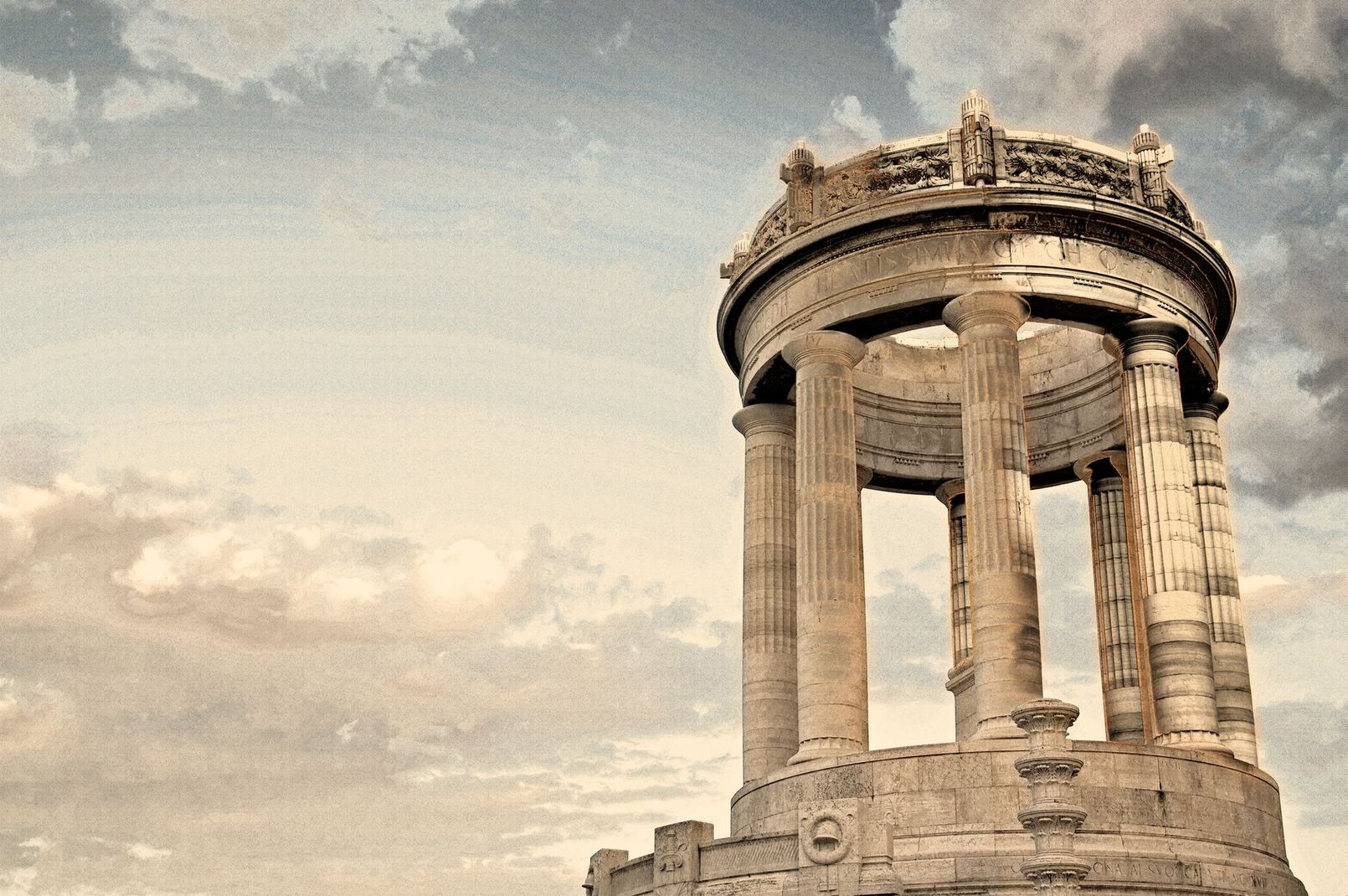 Antico monumento in pietra con colonne e sommità decorata, stagliato contro un cielo nuvoloso.