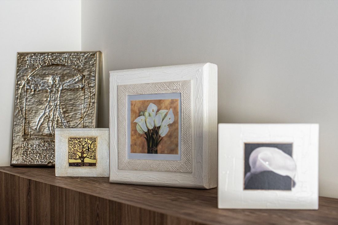 Tre foto decorative incorniciate sono esposte su una mensola di legno contro una parete beige.