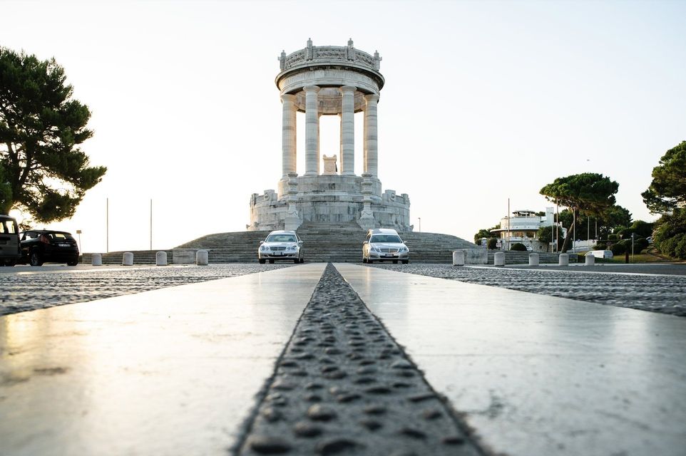 Monumento in pietra con colonne al centro di un ampio viale in una piazza aperta al crepuscolo