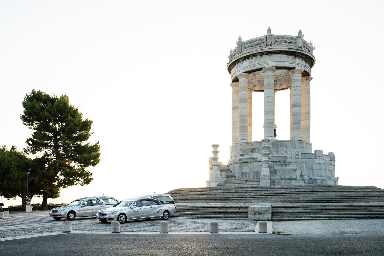Monumento in pietra con colonne accanto ad auto parcheggiate e un albero al tramonto