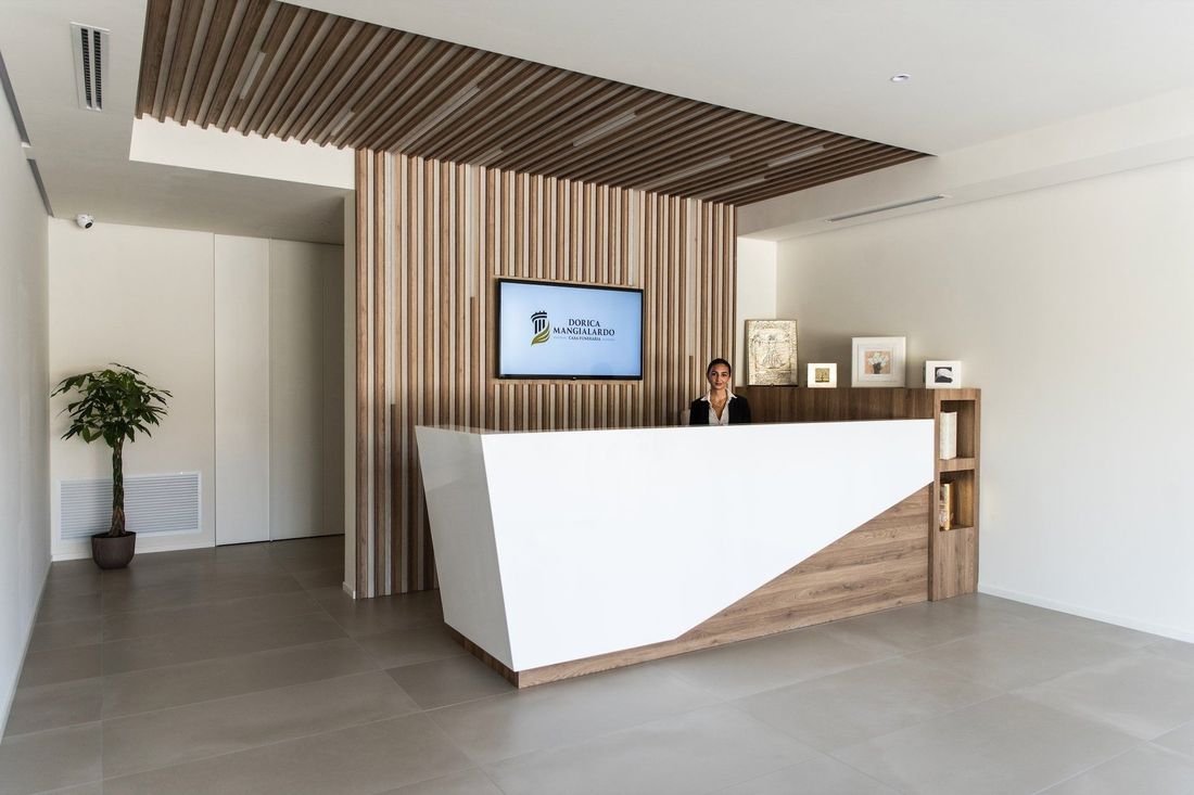 Banco reception moderno in una hall luminosa con soffitto a doghe di legno e pareti bianche.