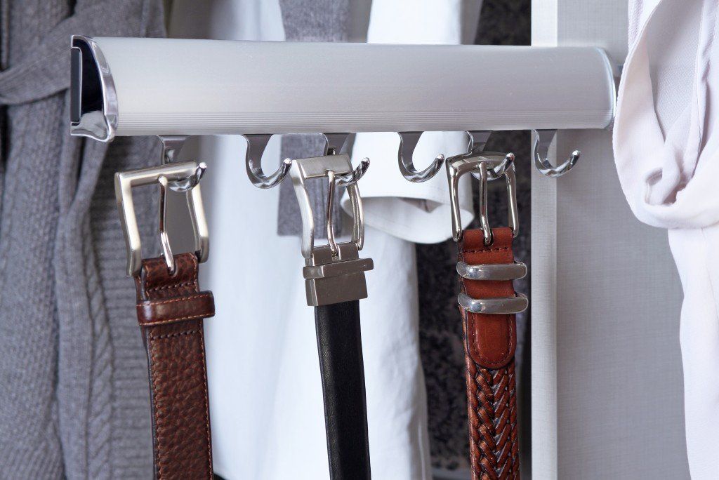 Silver belt rack holding three belts. Two are brown, one is black. Part of a closet.
