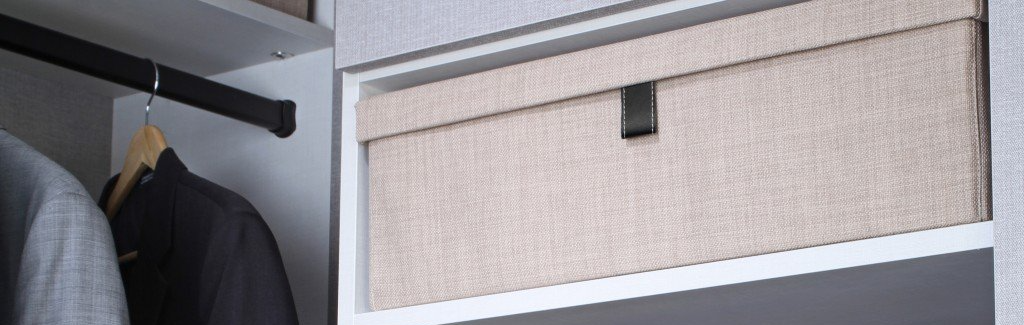 A closet with a black bar and a box on a shelf. The box is beige and has a black handle.