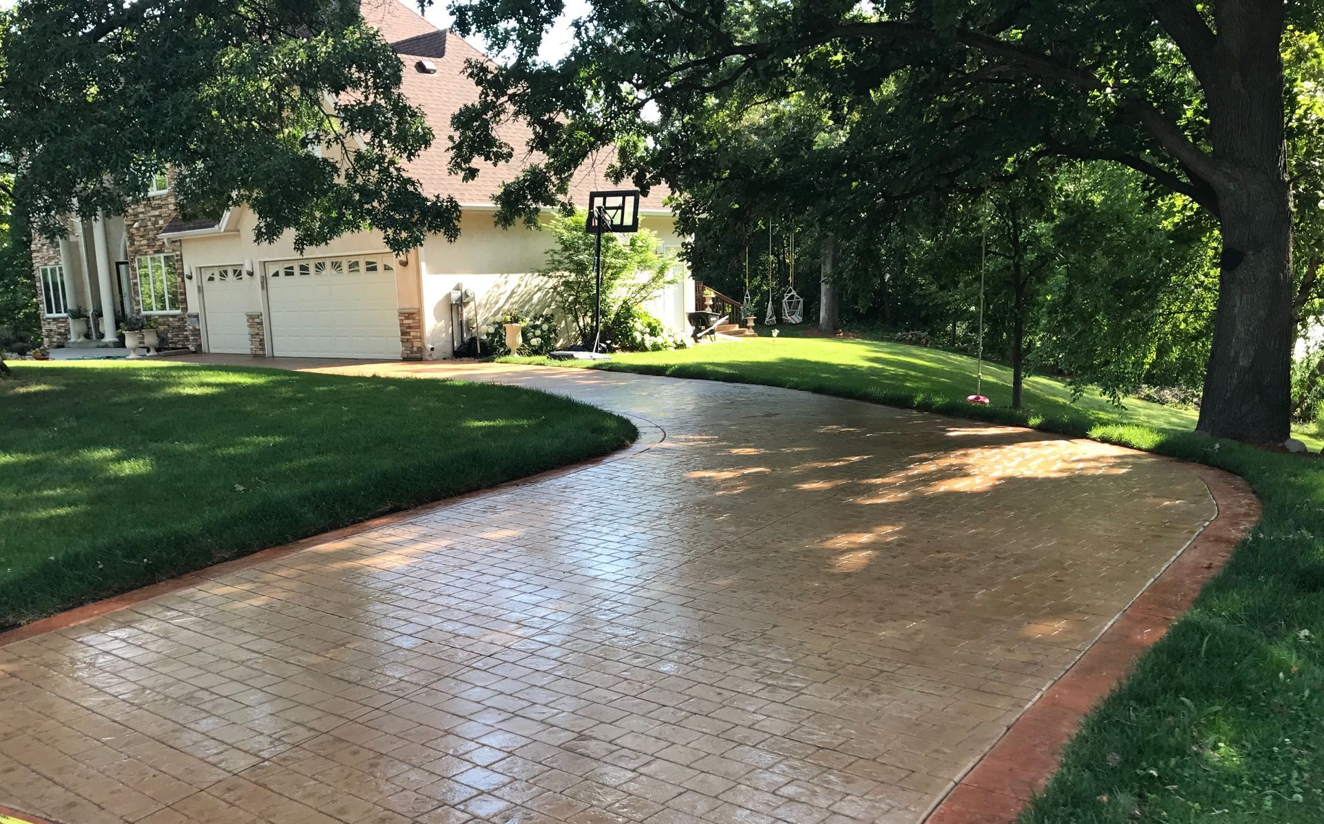 Brick driveway curving towards a house with a basketball hoop on a sunny day.