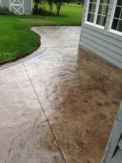 Stamped concrete patio with brown and tan hues, next to a house and green lawn.