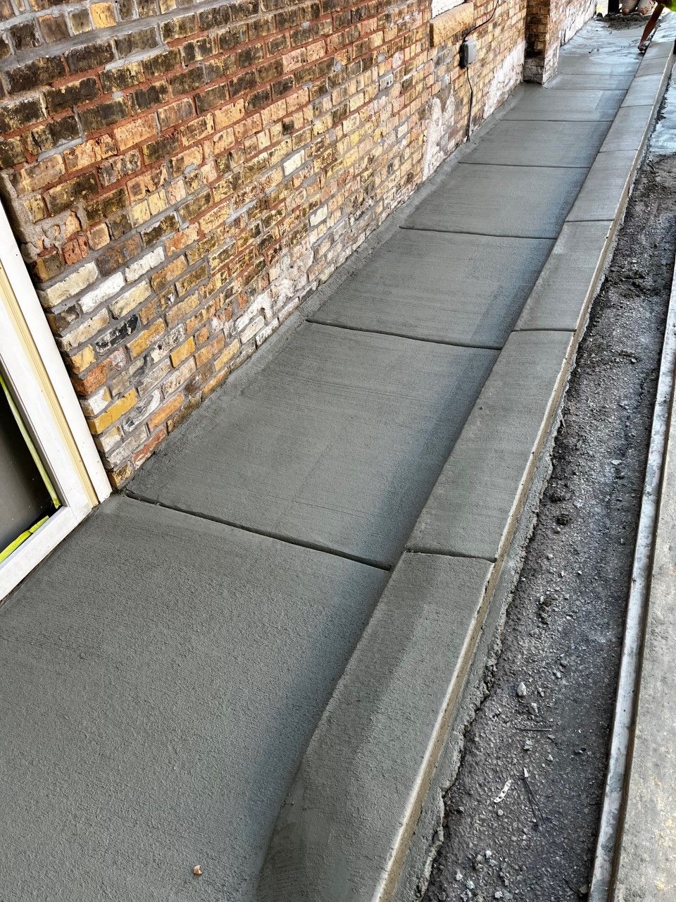 Newly poured concrete sidewalk with a brick building on the left.