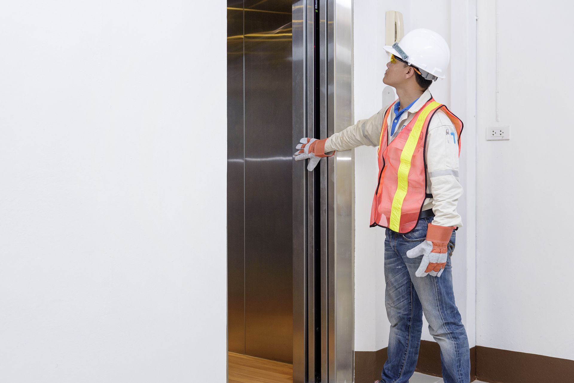 Construction worker opens elevator door, wearing safety vest, gloves, and hard hat