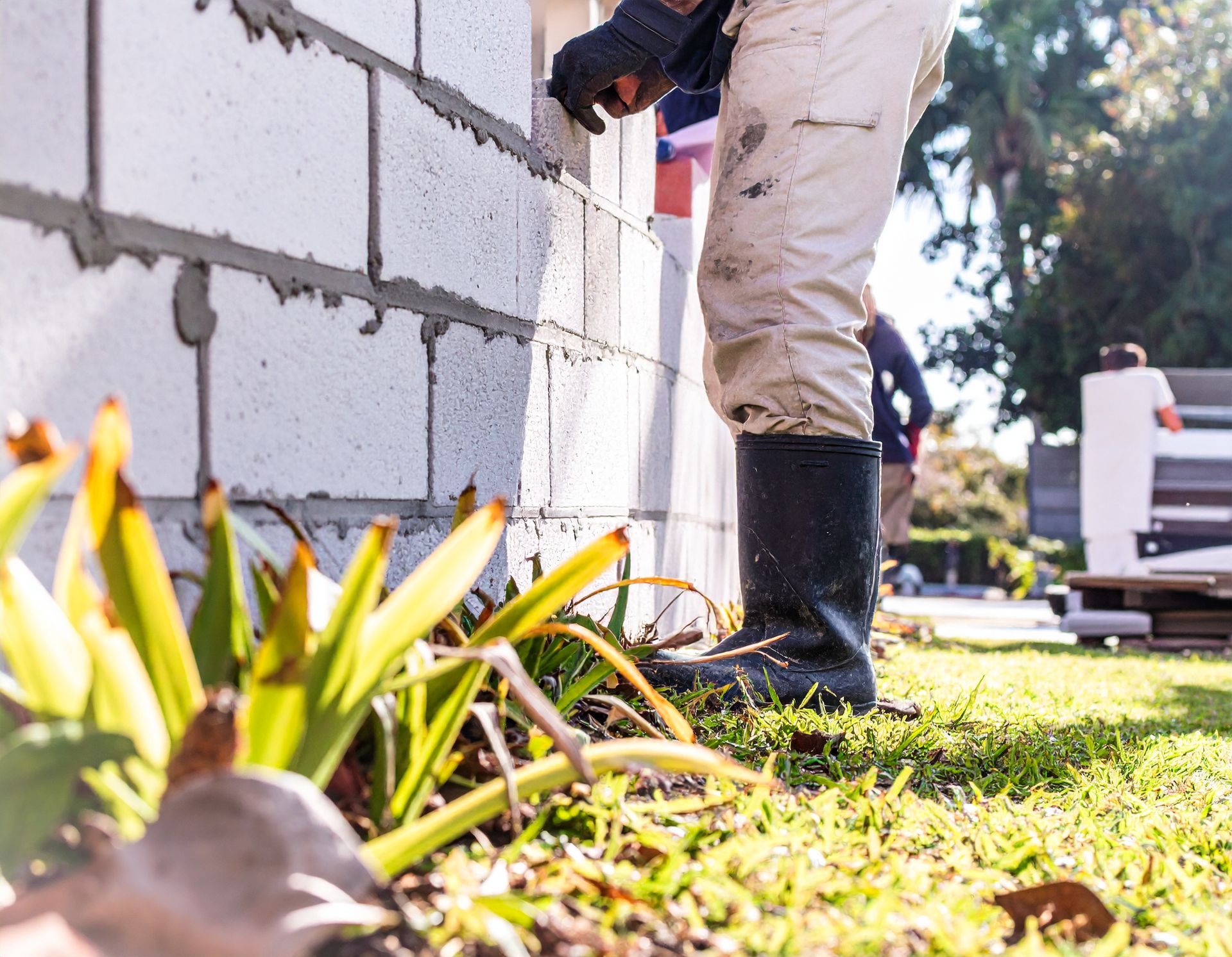 Worker standing beside a freshly built CMU wall along a lawn in Bushnell