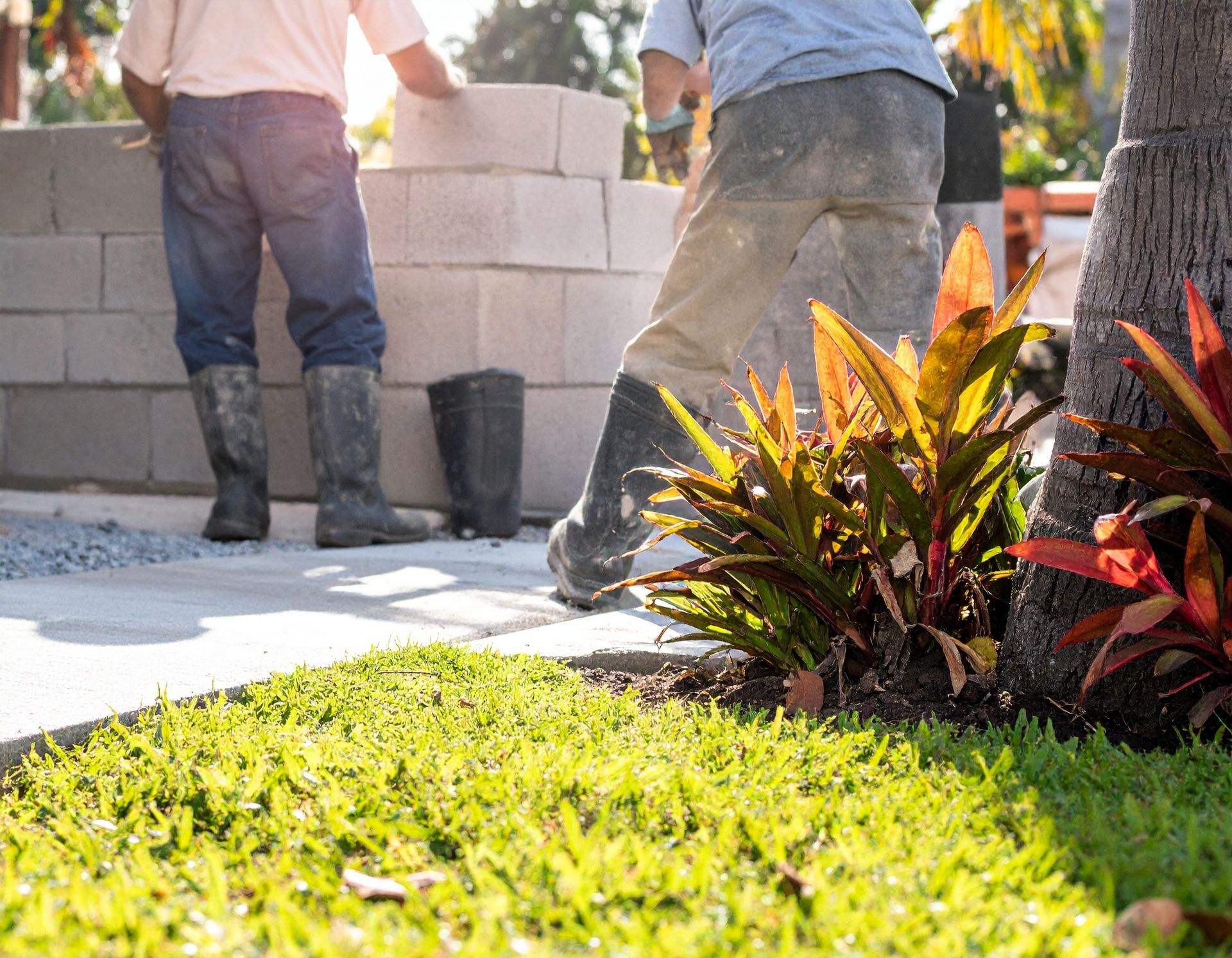 Crew laying concrete blocks for a home wall beside tropical landscaping in Bushnell