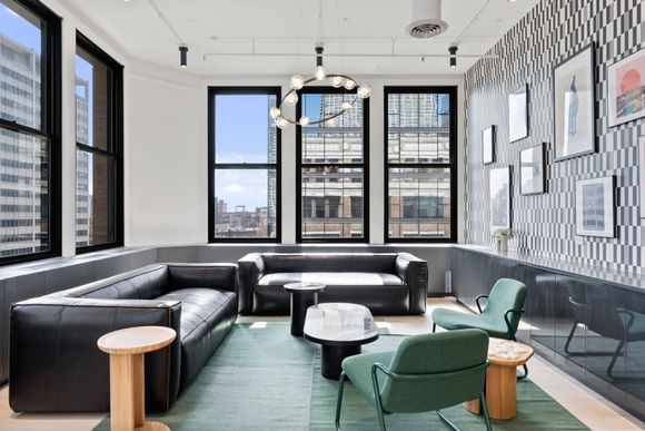 A modern lounge with black leather sofas, green armchairs, wooden side tables, and a gallery wall with patterned wallpaper.
