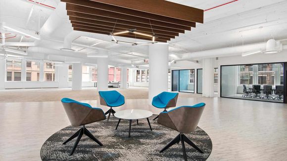 Modern open office lobby with four blue swivel chairs around a small white table on a circular patterned rug.