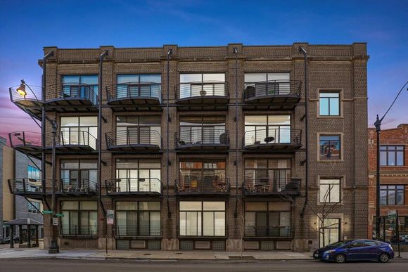 A four-story brick apartment building at twilight, featuring metal balconies and large windows on a city street.