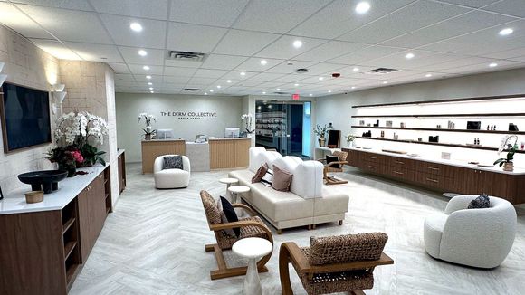 A modern, well-lit retail showroom featuring wood cabinetry, white armchairs, a central sofa, and shelves of footwear.