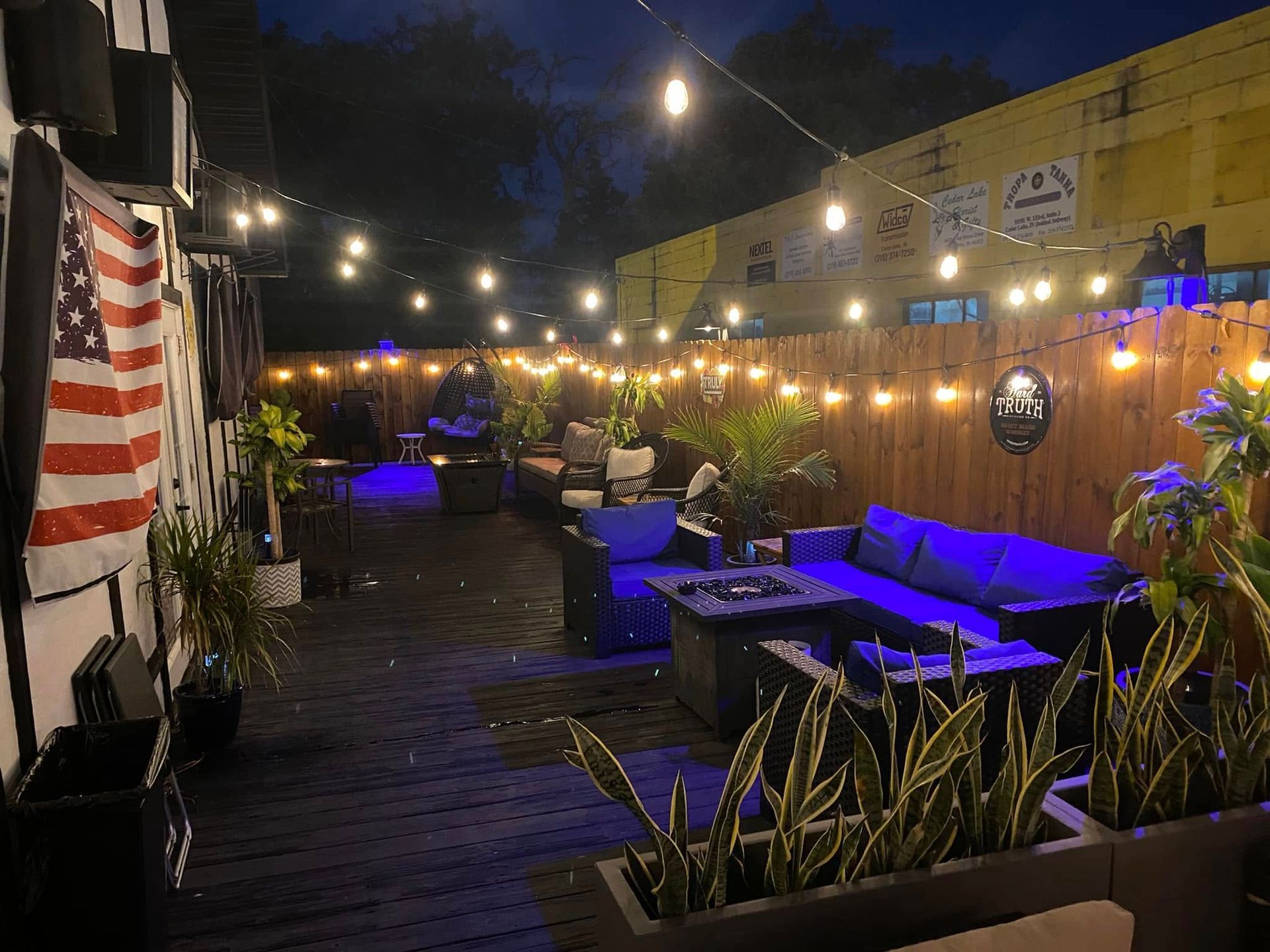 Outdoor patio at night with string lights, seating, and American flag.